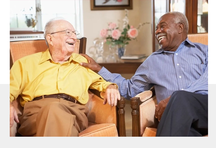 Two older men sitting in a chair and laughing.